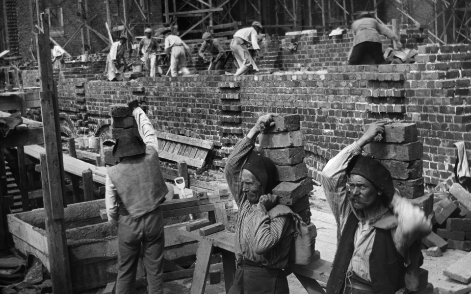Foto av män på 1910-talet som bär tegelstenar på ryggen.