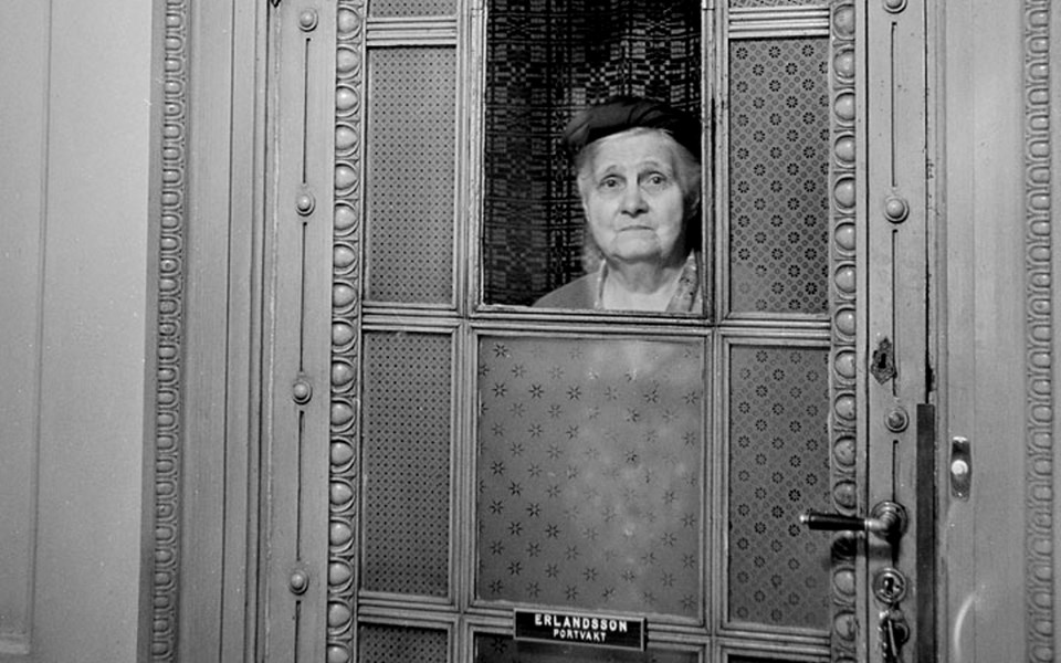 Äldre kvinna arbetar som portvakt i en port till ett lägenhetshus 1964. Foto.