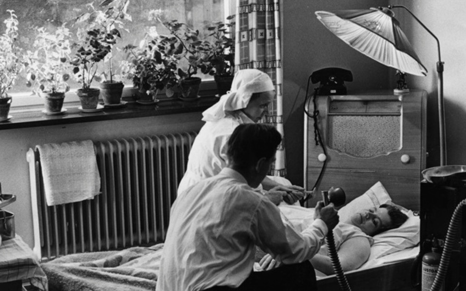 Foto. Barnmorska hjälper födande kvinna, mannen sitter bredvid.