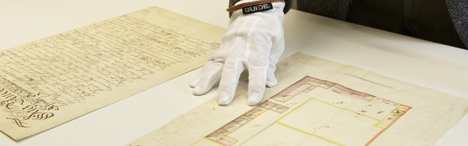 Person med vit handske som studerar en arkivhandling. Foto.